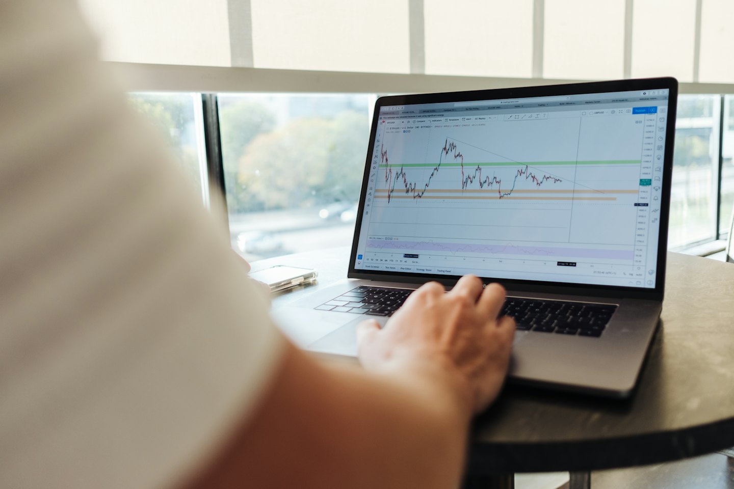 Person som tittar på finansiella diagram på en bärbar dator vid ett bord.